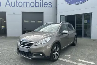 Peugeot 2008 champagne vue 3/4 avant droit, avec jantes alliage et rétroviseurs chromés devant un garage.