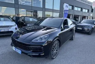 Vue 3/4 avant d'un Porsche Cayenne Coupé noir métal 2020, avec jantes alliage et calandre large, stationné devant un garage.