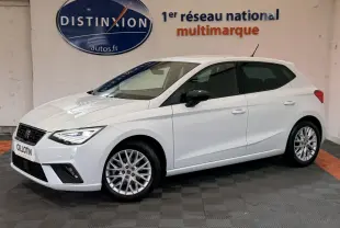 Vue 3/4 avant gauche d'une SEAT Ibiza 1.0 TSI 110 FR blanche avec jantes alliage et phares LED allumés.
