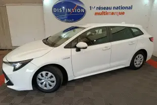 Vue de profil côté gauche d'une Toyota Corolla Hybride 122h Active blanche en version break, stationnée en intérieur showroom.