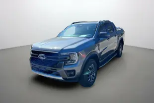 Ford Ranger 2.0 Wildtrak gris carbone en 3/4 avant droit, avec barres de toit et jantes alu 18 pouces.
