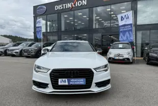 Vue frontale d'une Audi A7 Sportback blanche 2018 avec calandre noire et plaque « VÉHICULES OCCASIONS » devant un showroom.