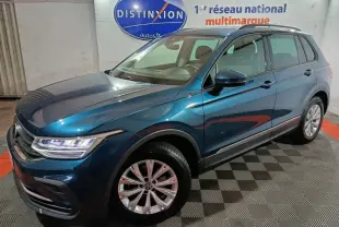 Volkswagen Tiguan bleu en 3/4 avant droit, avec jantes alliage et phares LED visibles en intérieur showroom.