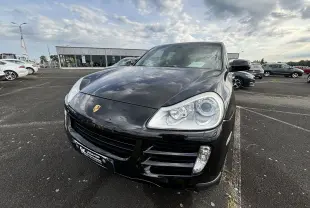 Vue 3/4 avant d'un Porsche Cayenne S noir brillant, mettant en valeur ses phares distinctifs et son logo Porsche sur le capot.