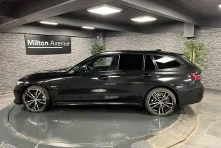 BMW Série 3 320e Touring noire vue de profil côté gauche avec jantes M Sport bicolores en intérieur showroom.