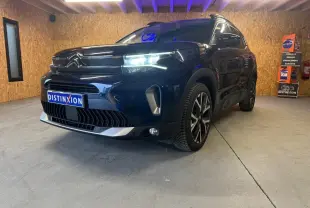 Vue 3/4 avant droite du Citroën C5 Aircross bleu avec barres de toit et jantes alu 18 pouces dans un showroom.