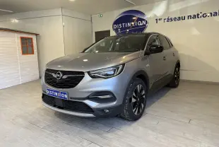 Opel Grandland X gris Himalaya vu en 3/4 avant droit, intérieur showroom avec logo Distinxion en arrière-plan.