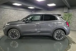 Vue de profil côté gauche d'un Fiat 500X gris avec jantes alliage 17 pouces dans un showroom intérieur.