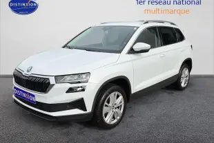 Vue 3/4 avant d'un Skoda Karoq blanc glacial avec jantes alu et barres de toit noires sur fond neutre.