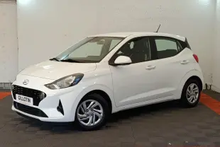 Hyundai i10 blanc vue 3/4 avant droit, avec calandre noire et jantes alliage argentées visibles.