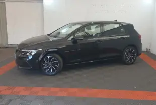 Volkswagen Golf noire vue de profil côté gauche, avec jantes alliage et phares LED visibles, stationnée en intérieur.