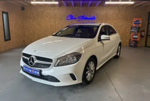 Mercedes Classe A 200D blanche vue de 3/4 avant droit dans un showroom avec mur en bois et enseigne bleue lumineuse.