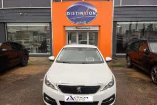Vue avant d'une Peugeot 308 blanche Banquise garée devant une concession avec un panneau orange Distinxion.