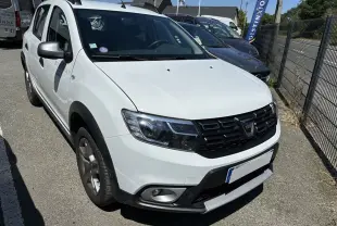 Vue 3/4 avant d'une Dacia Sandero Stepway blanche 2020 avec calandre noire et protections noires sur les ailes.