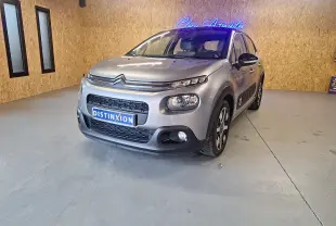 Citroën C3 gris en 3/4 avant droit dans un showroom, avec jantes alu et rétroviseurs noirs contrastants.