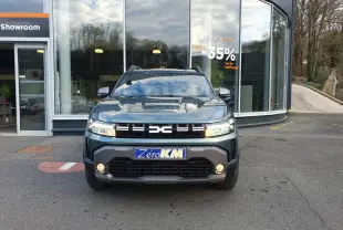 Vue frontale d'un Dacia Duster 2026 vert cèdre avec calandre noire et feux LED allumés devant un showroom.
