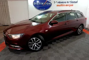 Opel Insignia break rouge vue 3/4 avant droit avec phares allumés dans un showroom intérieur.
