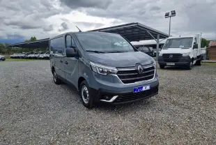 Renault Trafic Fourgon gris Highland en 3/4 avant droit sur parking gravillonné, avec calandre chromée et feux LED.