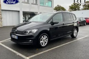 Volkswagen Touran noir intense nacré vu en 3/4 avant droit sur parking extérieur devant bâtiment moderne.