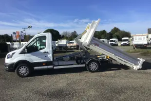 Vue de profil côté gauche d’un Ford Transit blanc avec benne basculante levée et bras de levage visible.
