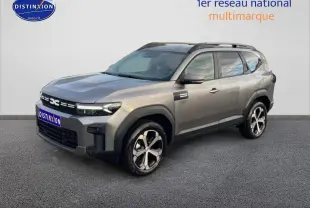 SUV Dacia Bigster gris schiste en 3/4 avant droit, avec jantes diamantées et barres de toit visibles.