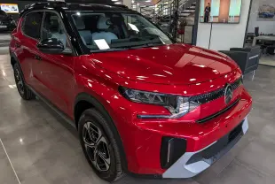 Vue 3/4 avant droite d'une Citroën C3 Aircross hybride rouge Elixir avec toit noir en showroom intérieur.