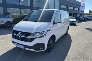Vue 3/4 avant droite d'un Volkswagen Transporter blanc 2022 avec jantes noires, stationné devant un garage.