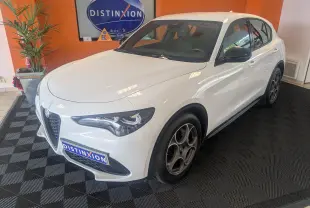 Vue 3/4 avant d'un Alfa Romeo Stelvio blanc 2023 avec jantes biton et rétroviseurs noirs en showroom.