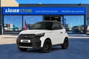 Vue 3/4 avant droite d’une Ligier JS60 Elite Revo blanc nacré avec toit noir et jantes noires devant un showroom Ligier.