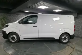 Opel Vivaro blanc en profil droit dans un showroom, avec roues tôles grises et poignées noires.