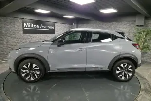 Profil côté gauche du Nissan Juke gris métallisé 2023 avec jantes bi-ton et poignées de porte couleur carrosserie.