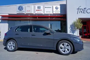 Profil côté gauche d'une Volkswagen Golf A8 2.0 TDI gris Urano garée devant un service multimarques.