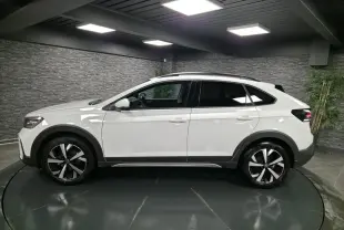 Profil droit du Volkswagen Taigo blanc 2024 avec jantes alliage 17 pouces et barres de toit noires dans un showroom.