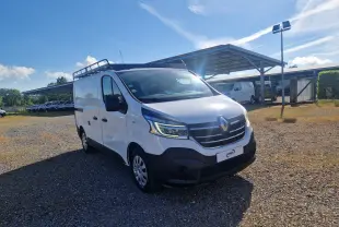 Renault Trafic Fourgon blanc vu en 3/4 avant droit avec galerie de toit, stationné sur un sol gravillonné.