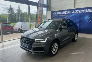Audi Q3 gris métallisé en 3/4 avant droit dans un showroom avec bannière publicitaire en arrière-plan.