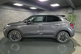 Profil droit d'un Fiat 500X gris avec jantes alliage 17 pouces et vitres surteintées dans un showroom.