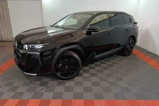 Vue 3/4 avant droit du SUV Citroën C5 hybride noir, avec jantes noires et phares LED allumés dans un garage.