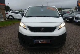 Vue frontale d'un Peugeot Expert Fourgon blanc avec calandre noire et phares allumés sur parking.