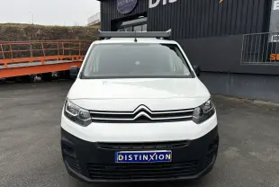 Vue avant d’un utilitaire Citroën Berlingo blanc avec pare-chocs noir et galerie de toit, stationné devant un bâtiment.