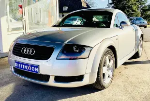 Audi TT Coupé gris vue 3/4 avant droit, avec calandre noire et jantes alliage cinq branches.