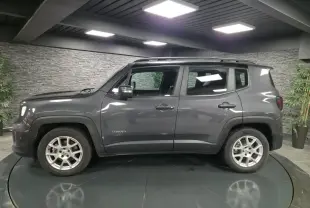 Jeep Renegade gris métallisé vu de profil côté gauche avec toit noir et jantes alliage 17 pouces en intérieur showroom.