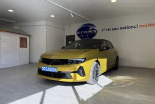 Opel Astra jaune vue 3/4 avant droit dans un showroom avec plaque "OCCASION" visible sur le pare-chocs.