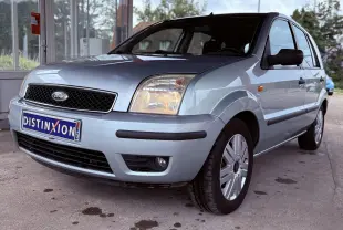 Ford Fusion bleu clair vue 3/4 avant droit avec phares allumés et plaque d'immatriculation Distinxion visible.