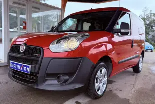 Fiat Doblo Cargo rouge vu en 3/4 avant droit, avec pare-chocs noir et phares allumés sous abri.