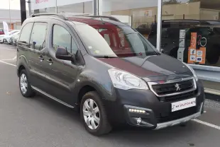 Peugeot Partner Tepee gris foncé vu en 3/4 avant droit, avec barres de toit et feux diurnes allumés.
