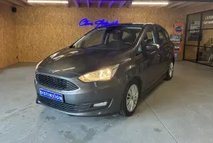 Ford C-MAX gris 3/4 avant droit en intérieur avec phares allumés et calandre hexagonale distinctive.