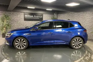 Profil côté gauche de la Renault Mégane hybride rechargeable bleu Iron avec jantes alliage 17 pouces en intérieur showroom.