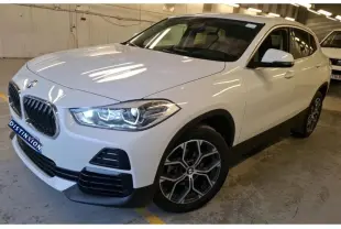 BMW X2 blanc vue 3/4 avant droit, jantes alliage 18'', rétroviseurs électrochromes et phares allumés.