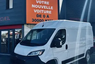 PEUGEOT Boxer Fourgon blanc vu en 3/4 avant droit devant un bâtiment commercial avec panneau orange.