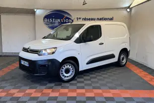 Vue 3/4 avant droite d’un utilitaire Citroën Berlingo blanc avec pare-chocs noirs et jantes acier en intérieur showroom.